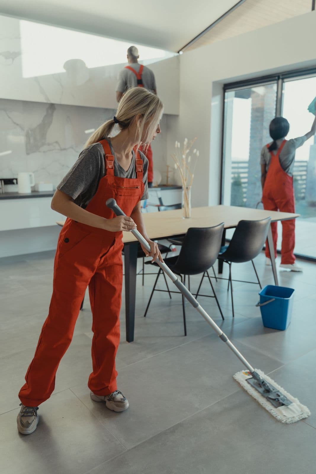 Cleaner mopping a floor while another wipes glass