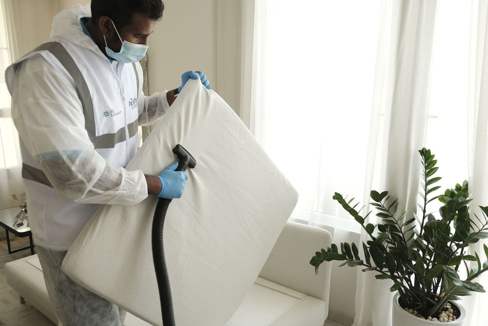 Technician in protective gear vacuuming a mattress